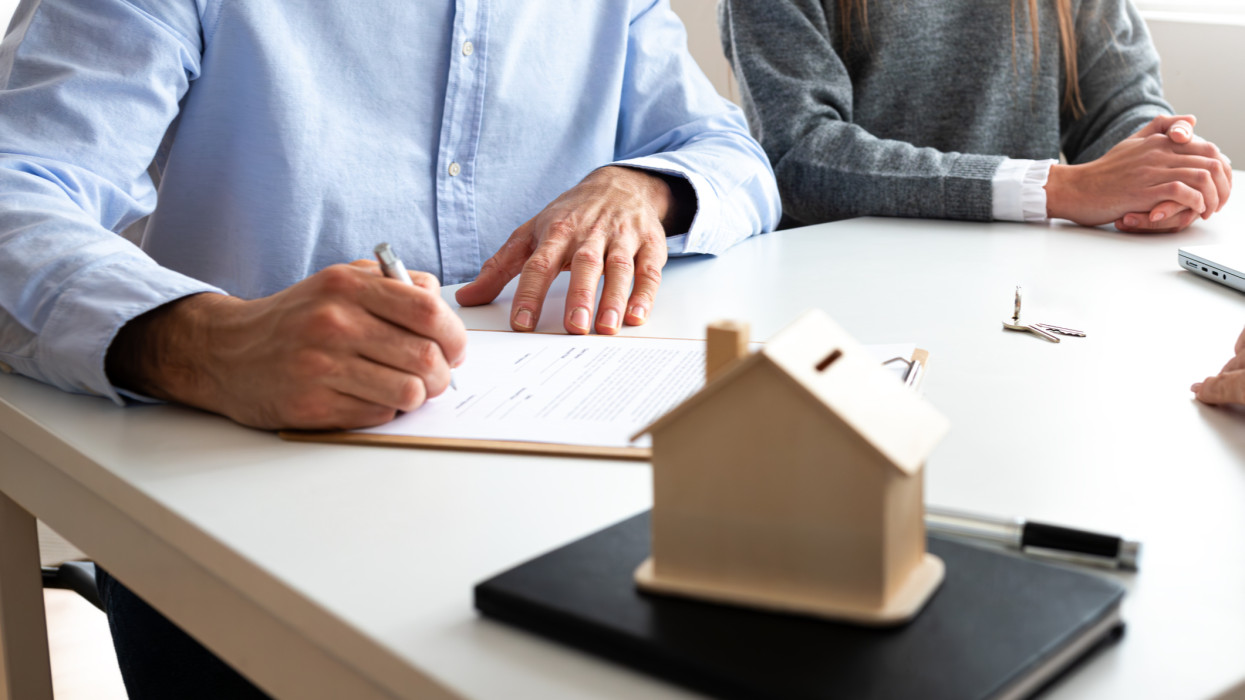 Unrecognizable man signing new home purchase agreement with wife. Young couple buying first home together. First time owners signing contract. Real estate concept.