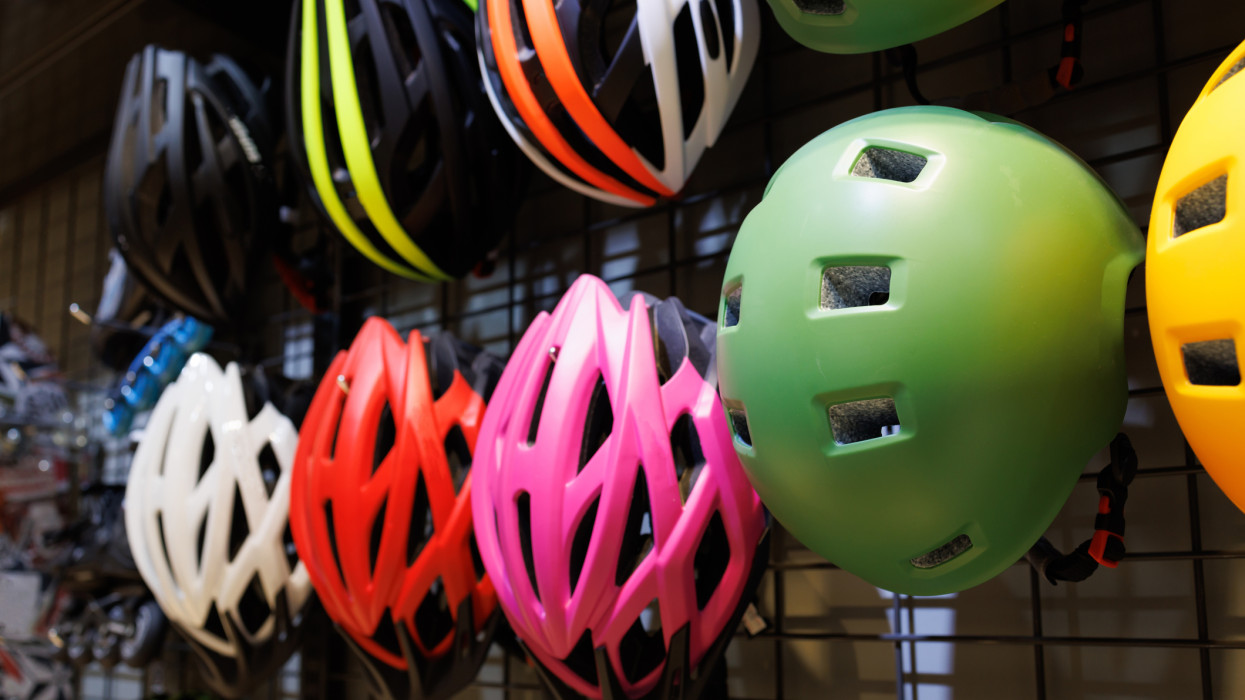 Bicycle safety helmets hang on metal wall in a bike shop.