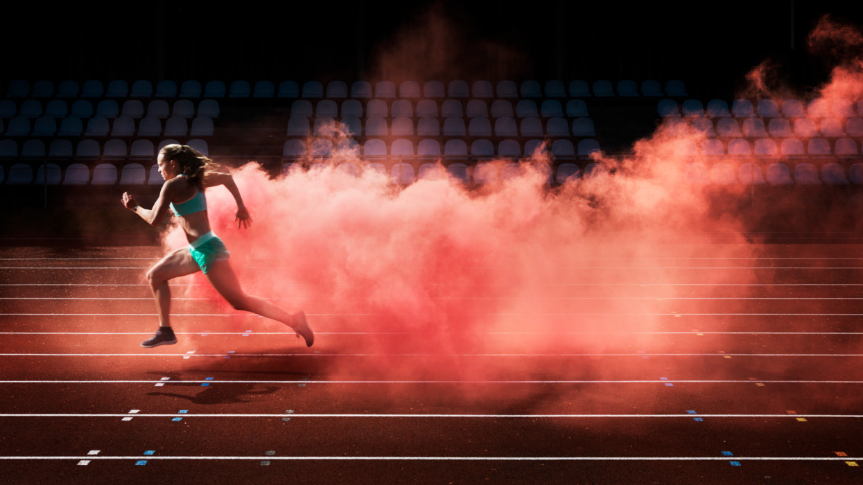 female athlete running in red smoke on stadium