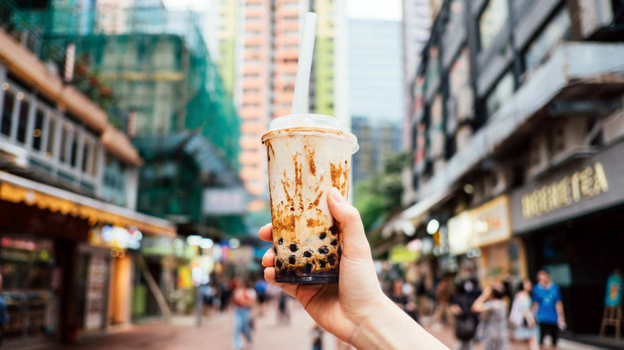 Human hand holding a bottle of iced cold bubble tea against city street in a hot summer day