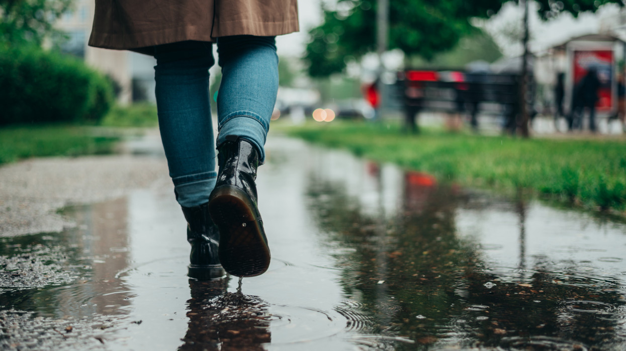 Woman legs walking on puddles while it rains in the city rainy storm weather