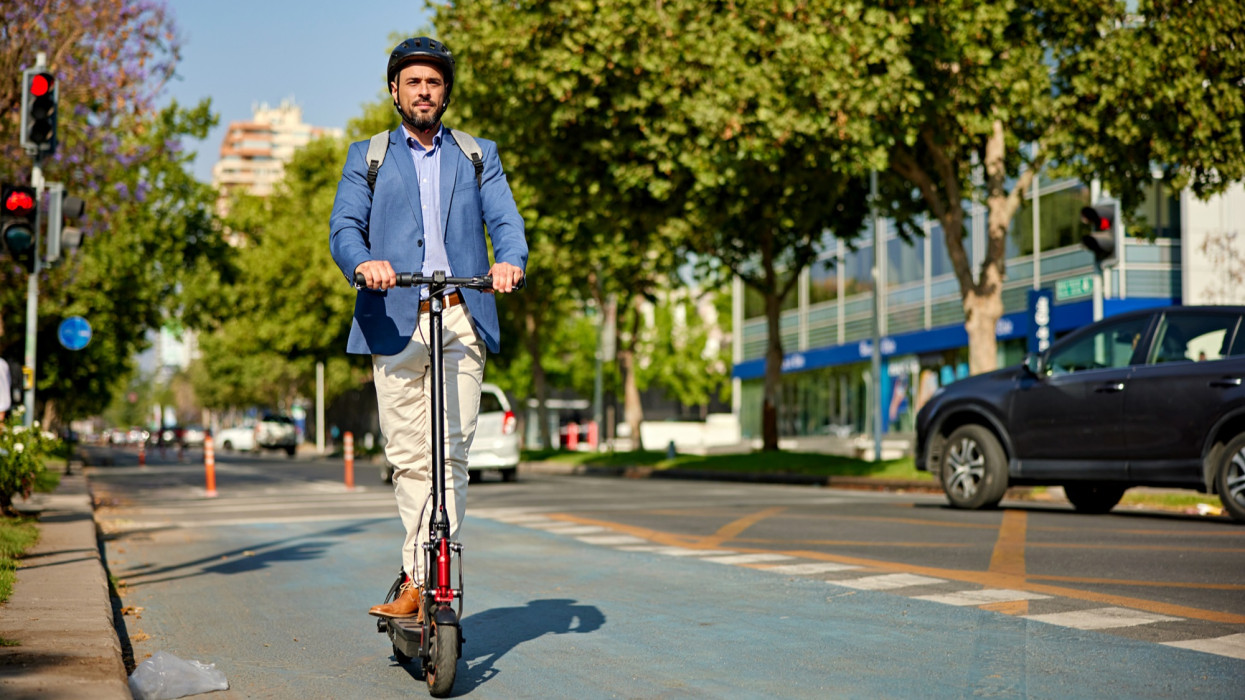 Full length front view of environmentally aware office worker wearing backpack, safety helmet, and riding in downtown district.