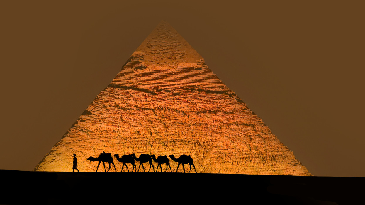 Composite image: A camel train and guide walking past great pyramids at Giza,