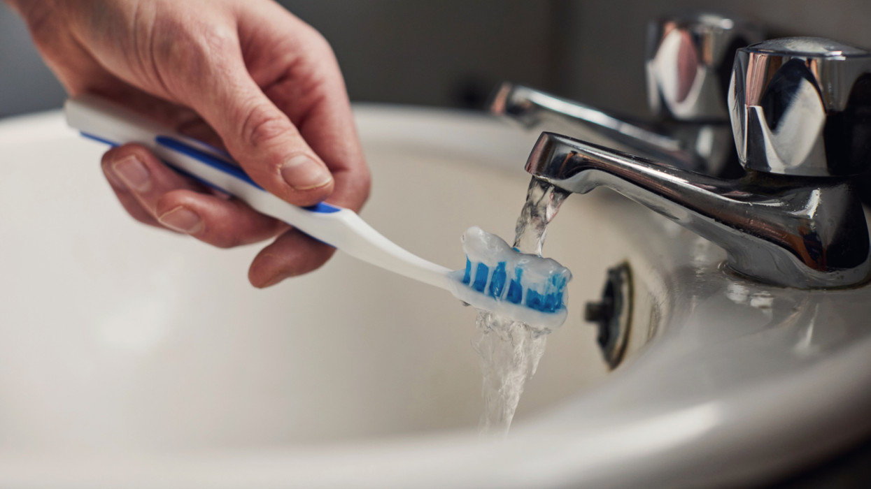 Woman holding a toothbrush under the water from the tap