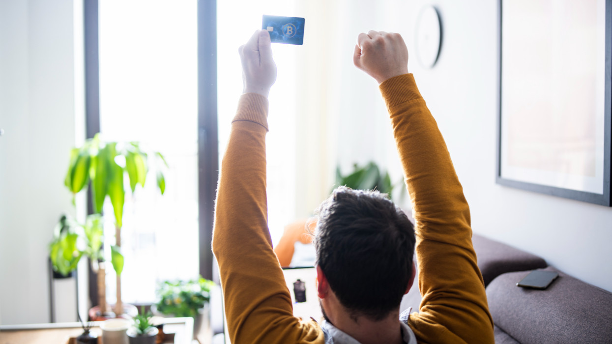 Rear view of happy unrecognizable man holding a credit card with his arms raised.