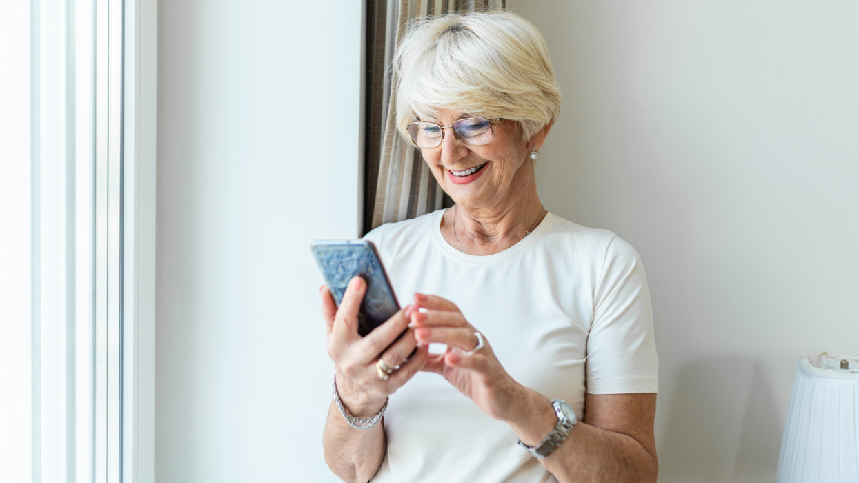 Portrait of cheerful senior woman using smartphone Photo of gray hair woman relaxing at home reading her text messages on her mobile phone with a quiet smile. Senior female texting or playing an online game on smartphone at home.