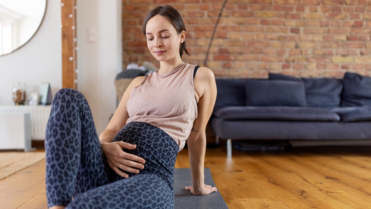 Pregnant woman resting with eyes closed and hand on stomach after prenatal workout at home. Expectant mother taking break after doing prenatal exercises at home.