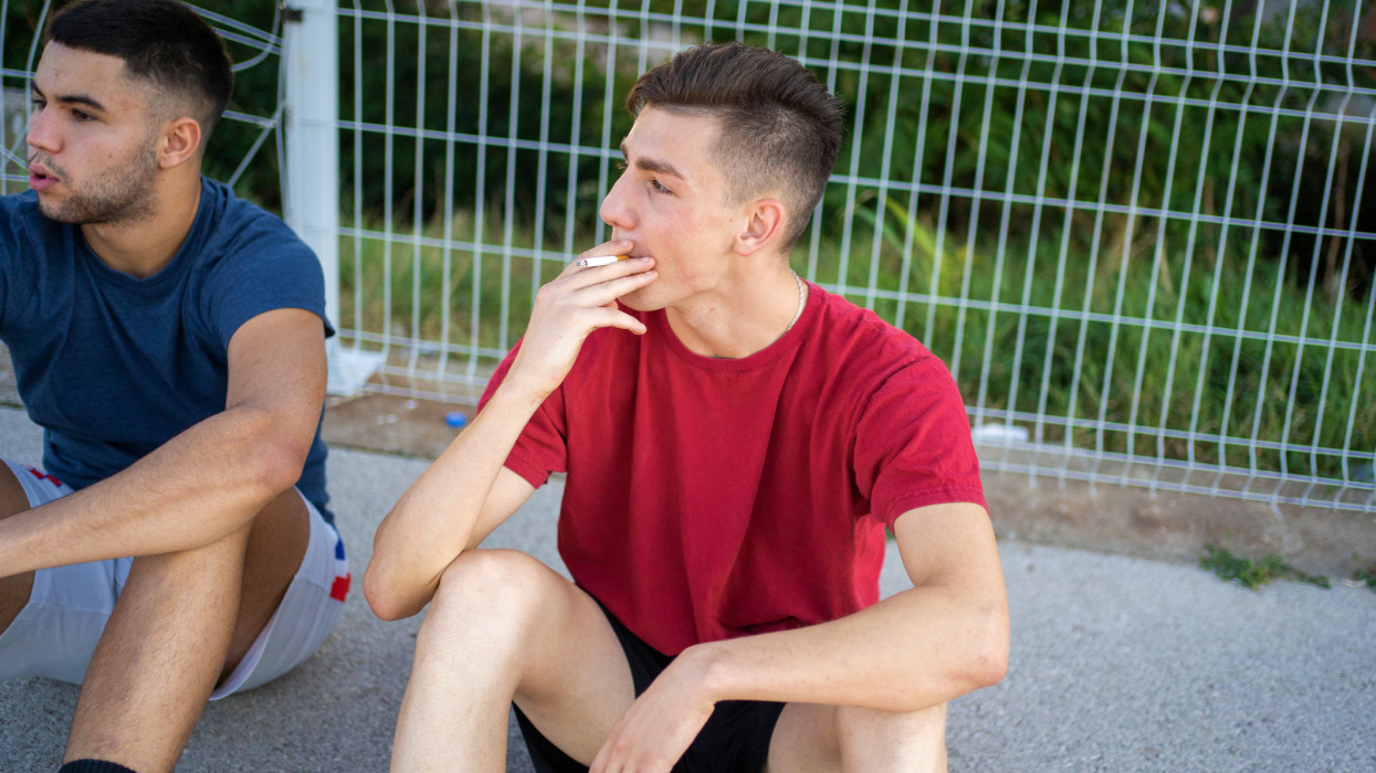 Unhealthy life. Two young athletes smoke a cigar while taking a break from basketball