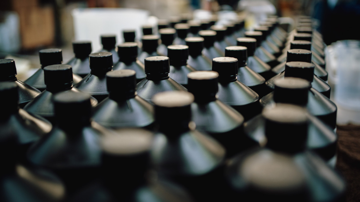 Many black bottles lined in up in a factory. Foreground blurred. / Female Focus Collection