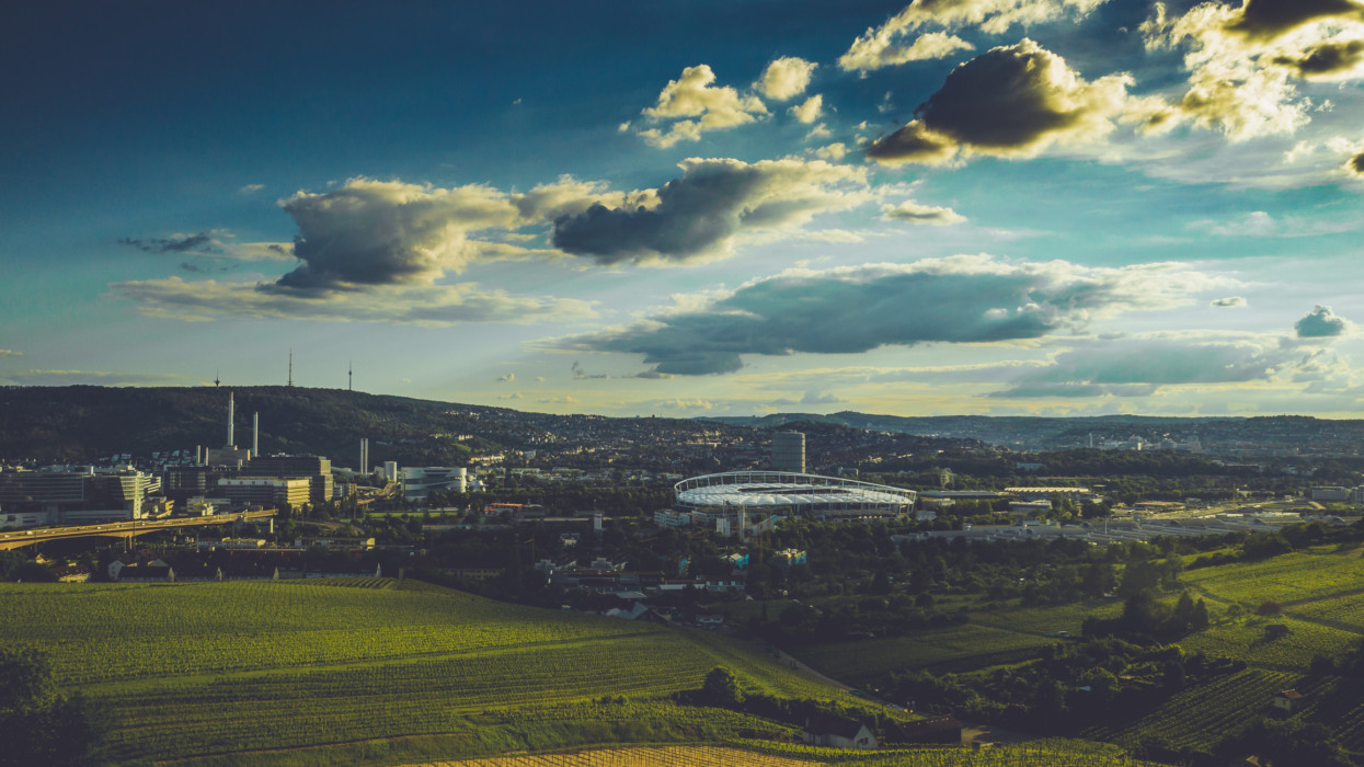 Stuttgart városa a Mercedes-Benz Arénával és a híres TV-toronnyal, kék égbolt és fehér felhők alatt.