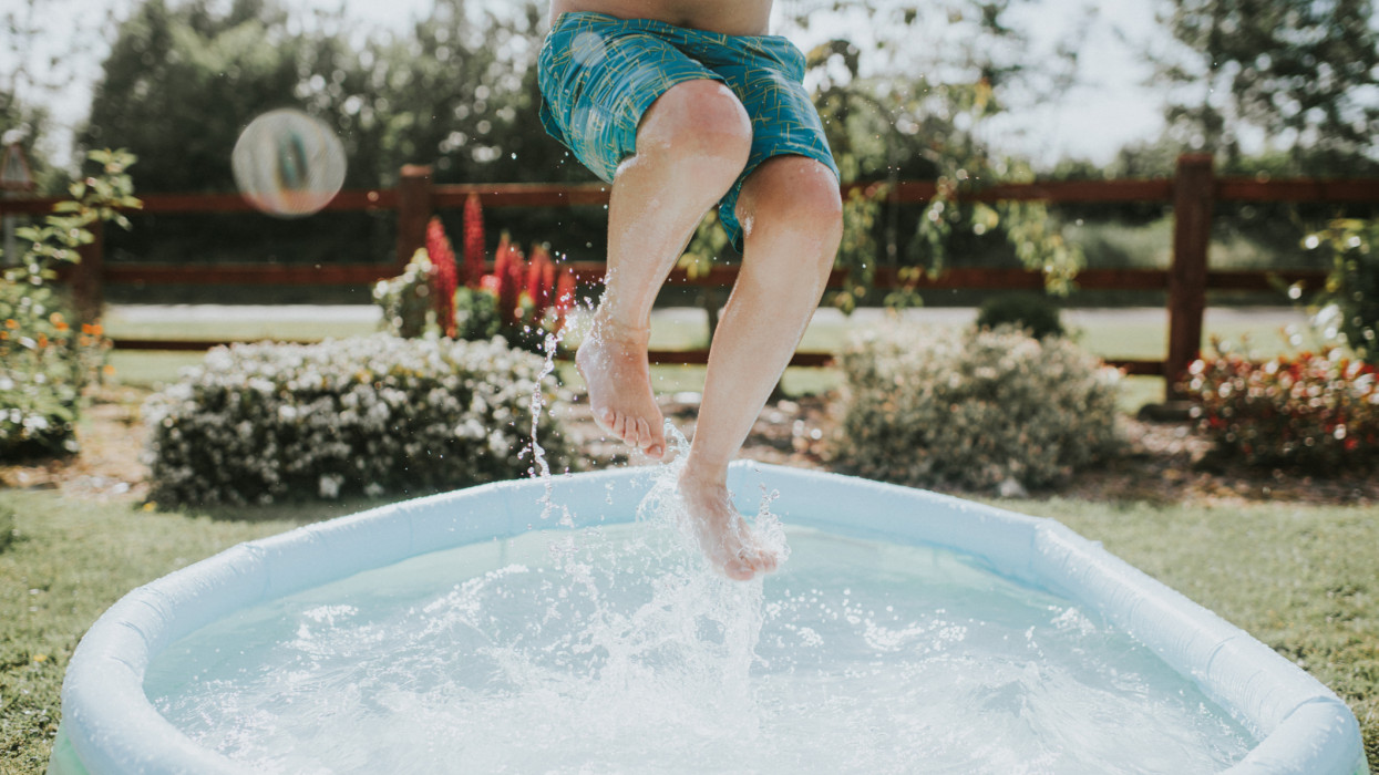 Úszónadrágos fiú ugrál és csobban egy kertben lévő medencében. Konceptuális, másolati lehetőséggel.