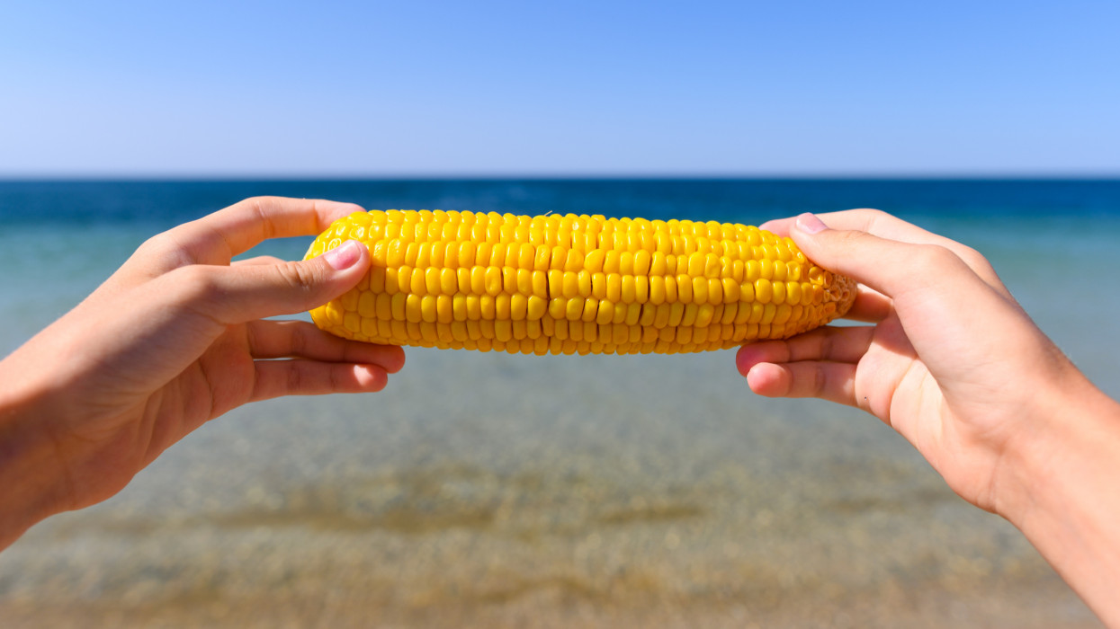 Delicious corn in childrens hands on the background of the sea.