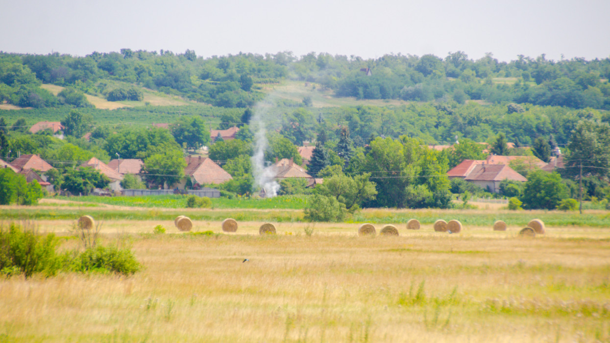 Landscape of rural HUngary with Round haybales and a small village in the background.