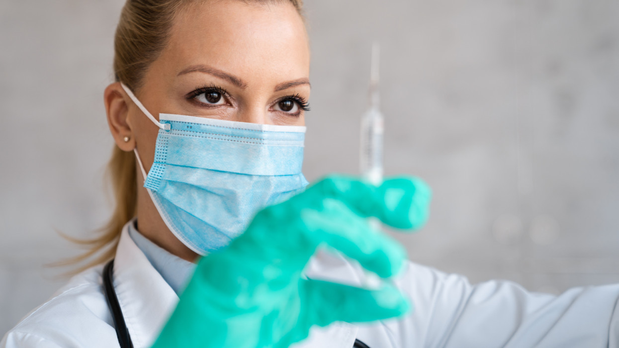 A female doctor who is wearing medical exam gloves and a face mask is ready to administrate the injection.