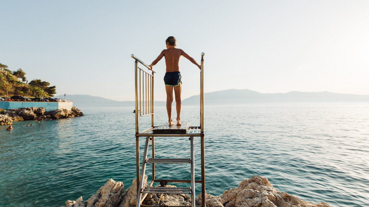 Young boy climbing on a diving platform and prepare to jump in to the sea
