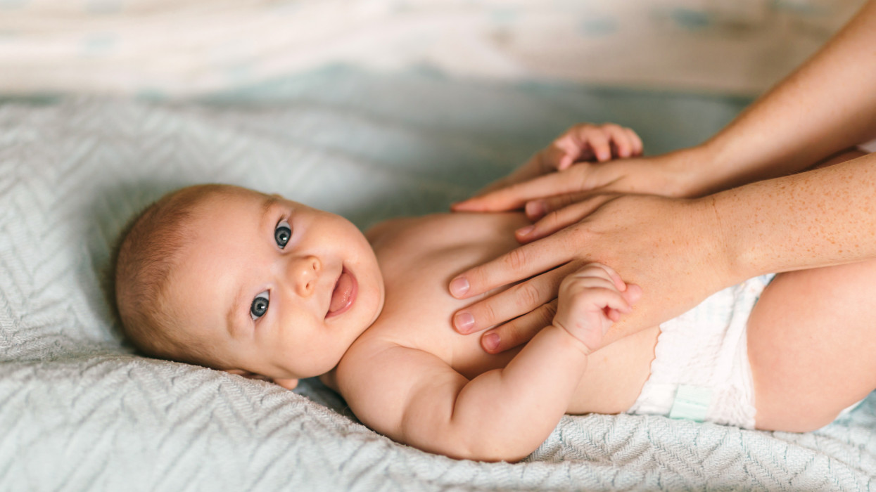 Masszázs a babának. Négy hónapos baba mosolyogva tornázik