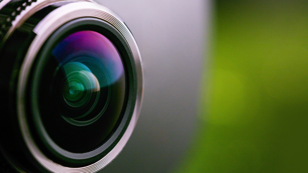 Zöld háttérvilágítású kamera objektív. A fényképezőgép lencséjének oldalnézete zöld háttérrel. Zöldkamera objektívje közelről. Tiszta vörös