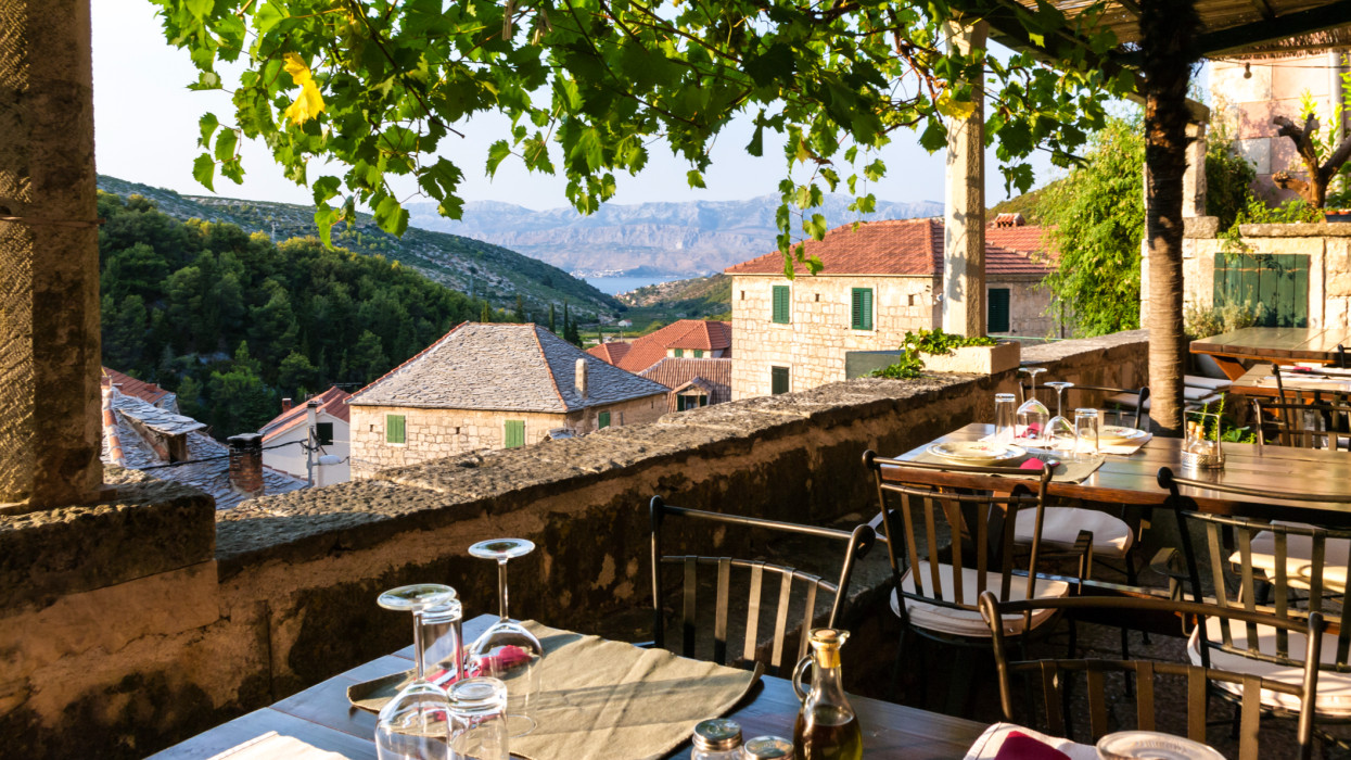 Terrace with tables and chairs with beautiful views of the town, sea and mountains. Dol - small town on Brac Island, Dalmatia, Croatia. Tourism.