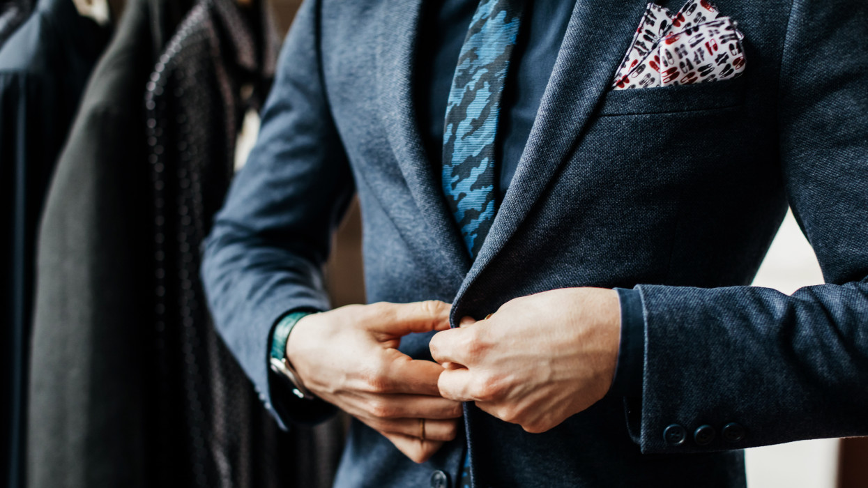 A close-up of a man buttoning up a suit while shopping in a menswear store.