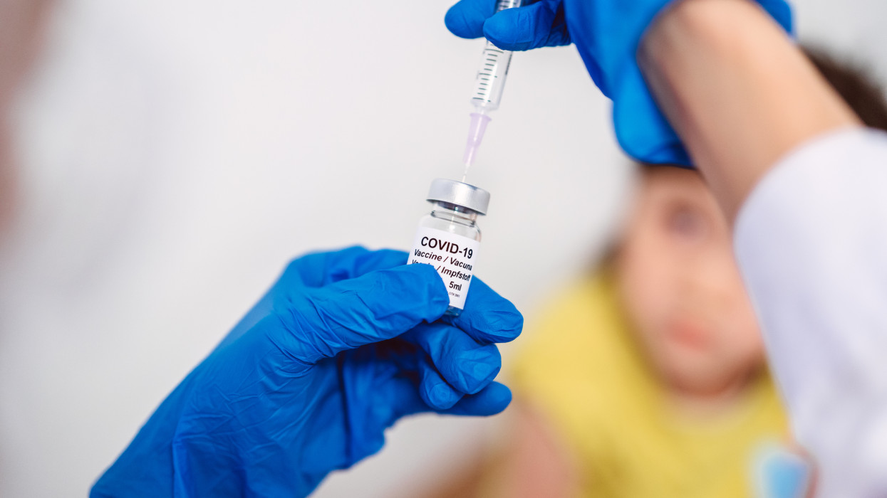 Medical doctor in protective gloves filling injection syringe with COVID-19 vaccine and ready to give kid girl Covid-19 vaccination.