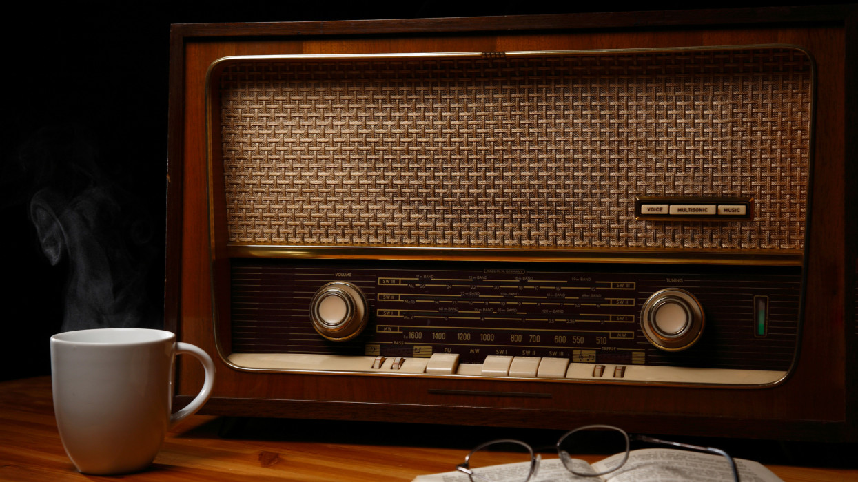 1950s valve radio with steaming mug of hot drink in-front of it and open book with reading glasses on top.