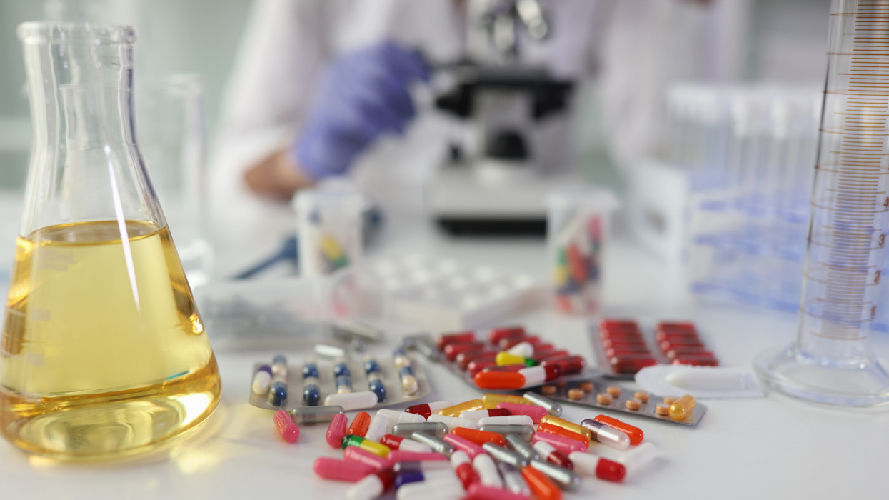Tabletták és sárga folyadék egy lombikban egy asztalon a laboratóriumban, közelkép. Gyógyszerek kémiai elemzése