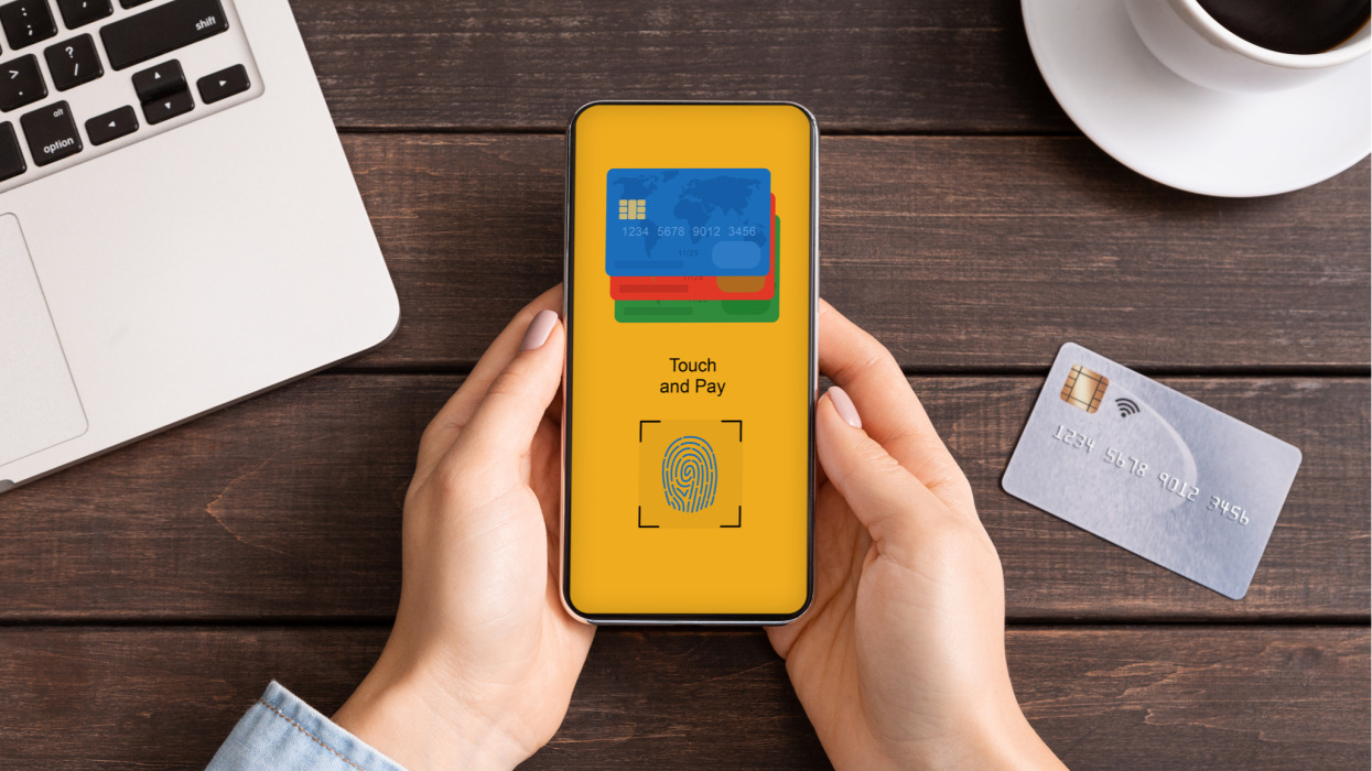 Unrecognizable business woman paying for goods and services online with Touch ID, using mobile phone while working in office, creative image for biometric authentication, payment systems concept