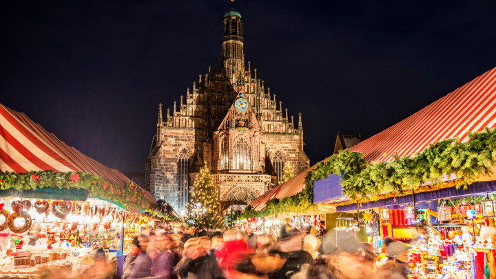 Huge crowd of people moving over NurembergÂ´s world-famous christmas market (Christkindlsmarkt) at night, passing colorful illuminated christmas decoration and food stalls. NurembergÂ´s landmark Frauenkirche (Church of our Lady) can be seen in the back.