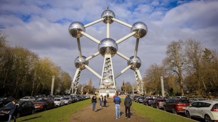 Brussels, Belgium - December 3, 2023: People stroll towards the Atomium in Brussels, admiring its unique architectural design and the clear blue sky overhead, with cars lining the nearby path.