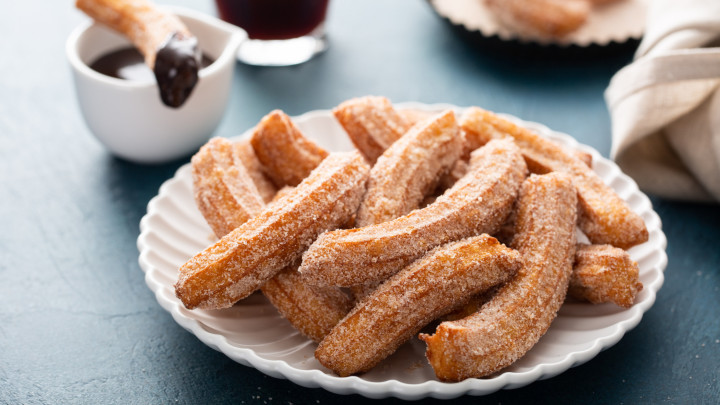 Házi készítésű churros fahéjas cukorral egy tányéron, csokoládémártással tálalva